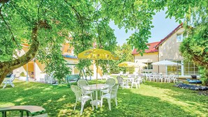 An outdoor seating area with tables and chairs, surrounded by trees and a building with a red roof. - 4 bedroom cozy home in Grzybowo (Grzybowo)