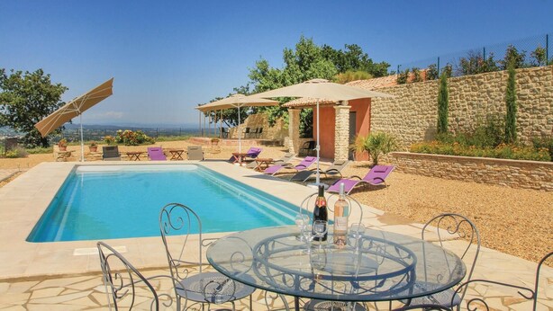 Piscina con sillas de descanso y una mesa con bebidas, rodeada de muros de piedra y vista al mar.