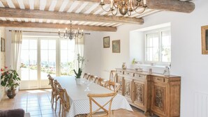 Un comedor con una mesa larga, sillas de madera, una araña y vistas a través de un ventanal.