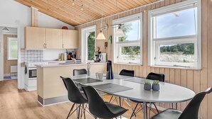 Una cocina moderna con armarios de madera, una zona de comedor con una mesa redonda y sillas, y ventanas amplias con vistas al exterior.
