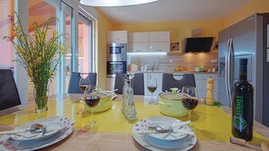 A dining area with a table set for two, a bottle of wine, and a vase of flowers. - Awesome home in Betiga (Betiga)