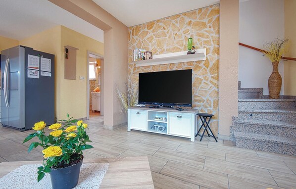 A living room with a stone wall, a flat-screen TV, a white entertainment unit, a kitchen with a refrigerator, and a staircase. - Awesome home in Betiga (Betiga)