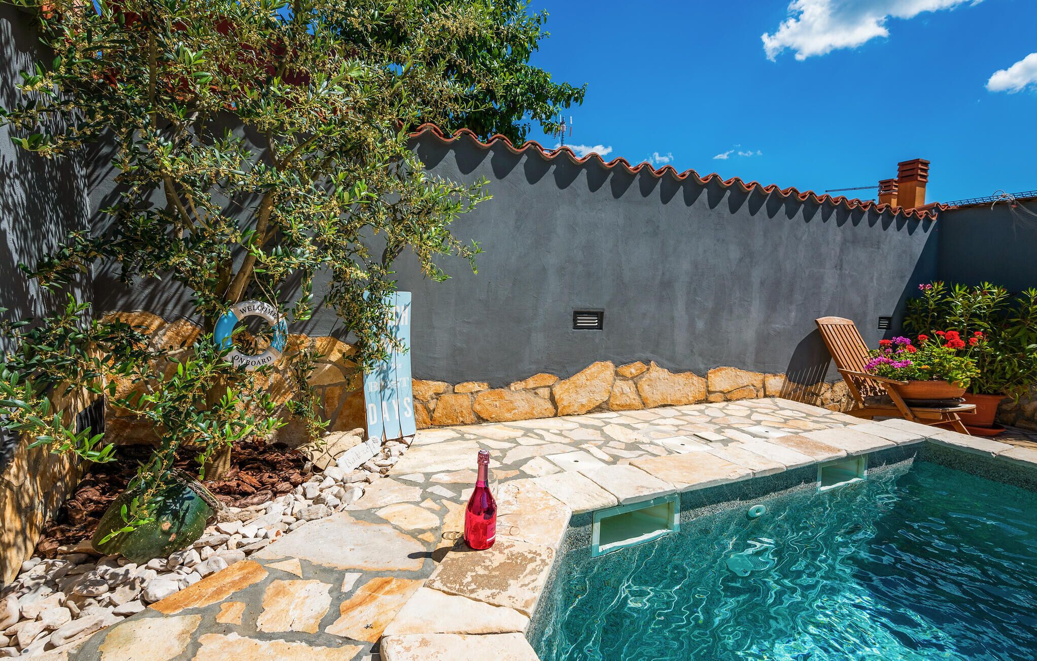 A poolside area with a stone patio, a small pool, and a wall with a tiled roof.