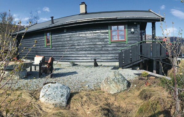 A rustic wooden cabin with a curved roof, a small porch, and a stone pathway leading to the entrance.