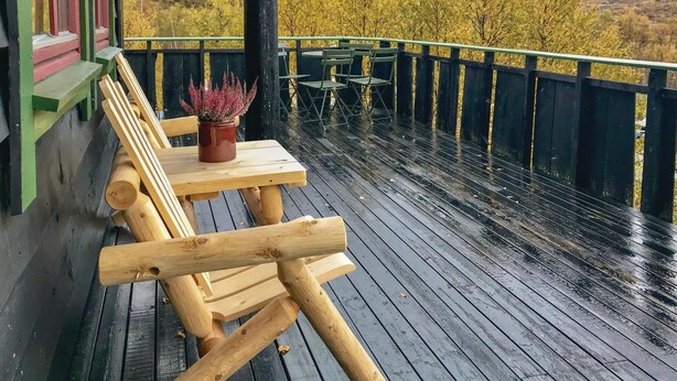 Una terraza de madera con un banco y una mesa, con vista a un cuerpo de agua y follaje otoñal.