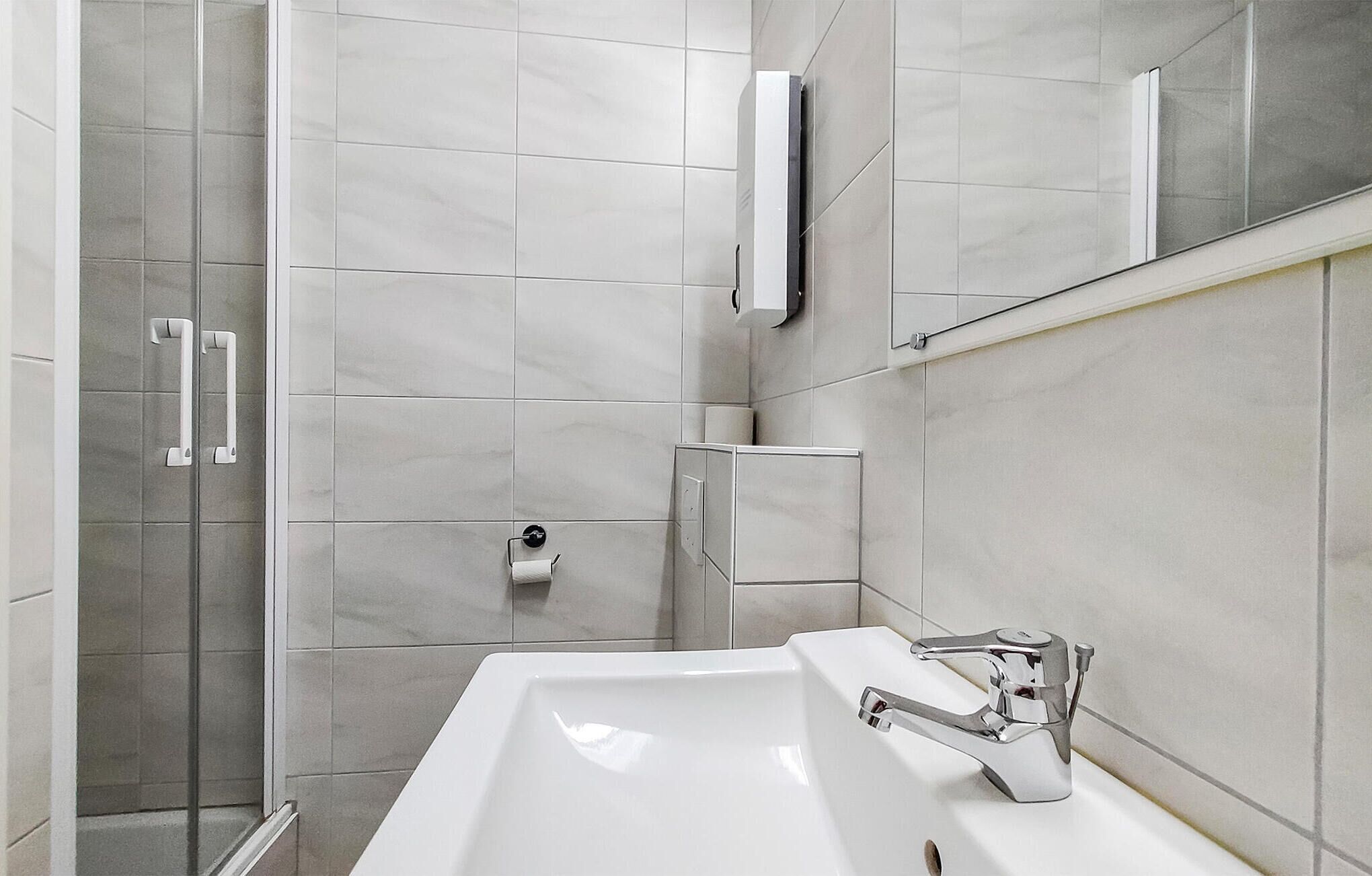 A modern bathroom with a glass shower enclosure, a white sink, and a mirror above the sink.