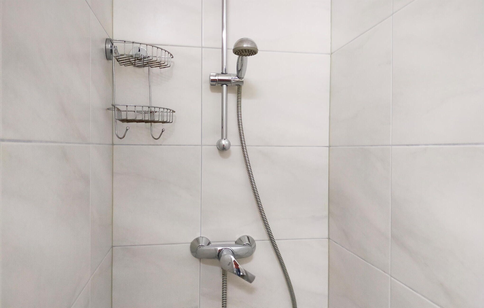 A shower area with a handheld showerhead, a fixed showerhead, and two metal shower trays.