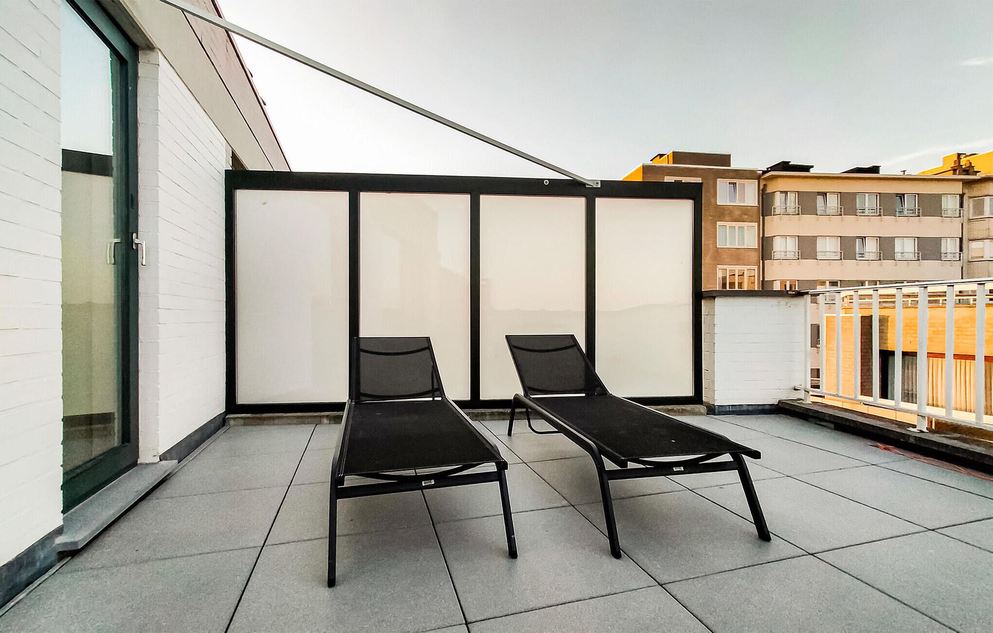 A balcony with two black lounge chairs and a glass partition.