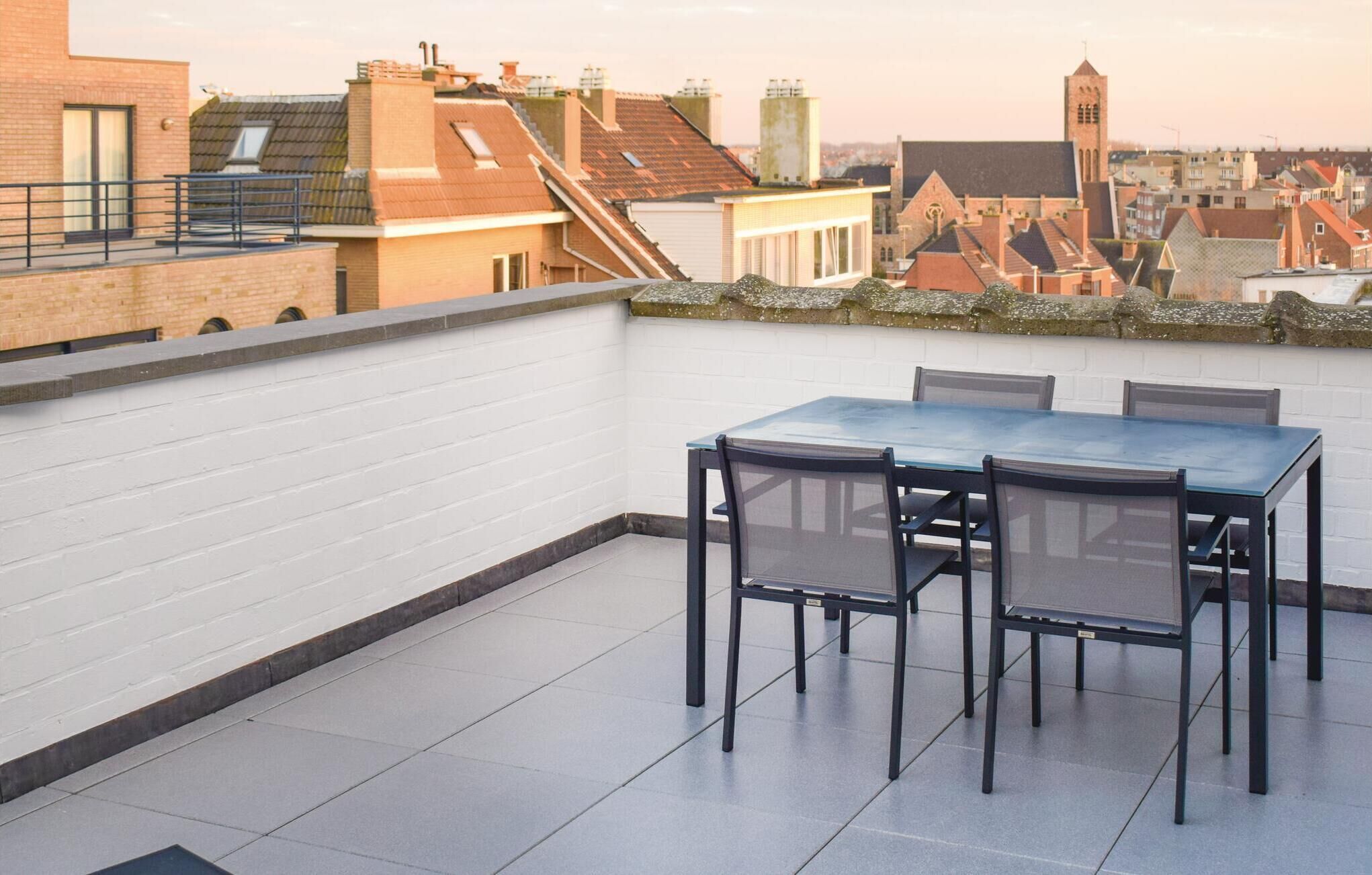 Une terrasse sur le toit, avec une table et des chaises, des murs en briques blanches et une vue sur le paysage urbain en arrière-plan.