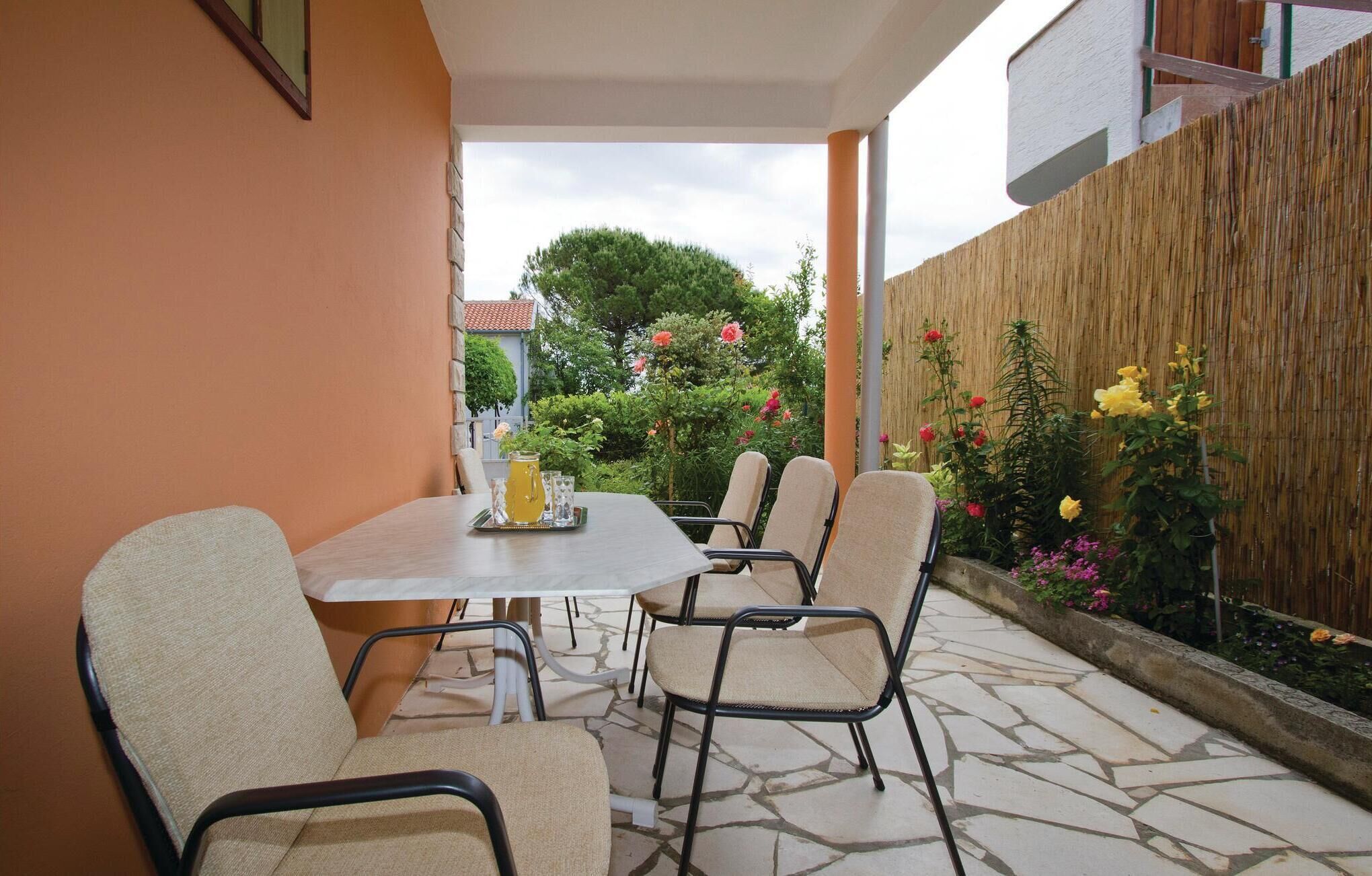 An outdoor patio with a table and chairs, surrounded by a bamboo fence and flowering plants.