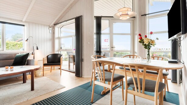 A spacious room with a large dining table, chairs, a sofa, and a TV. There are large windows providing natural light and a view of the outdoors. - Nice home in Rønde with WiFi (Rønde)