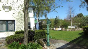 A house with a garden, a green outdoor water pump, and a white building in the background. - Apartment Type 1 - Meutzner Trassenheide, "Villa Seute Deern" (Trassenheide)