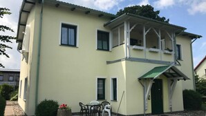 A two-story building with a balcony, a covered porch, and a small patio area with outdoor furniture. - Apartment Type 1 - Meutzner Trassenheide, "Villa Seute Deern" (Trassenheide)