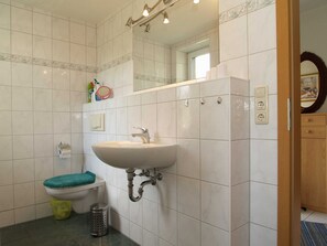 Une salle de bain avec un lavabo blanc, des toilettes, une poubelle et un miroir.
