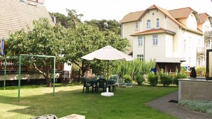 A residential backyard with a lawn, a swing set, a table with chairs, and a large umbrella. - Fritz-Reuter-Str. 10a. Curr. FR-10 - Fritz-Reuter-Str. 10a (Kühlungsborn)