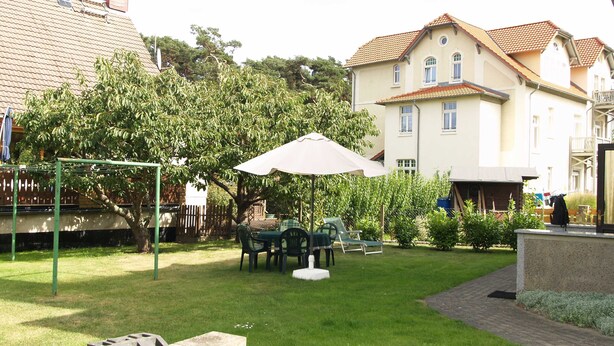 Un patio trasero residencial con césped, un conjunto de columpios, una mesa con sillas y un paraguas grande.