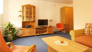 Una sala de estar con televisor, armarios de madera, sofá y una mesa.