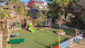 A fenced backyard with a swing set, slide, trampoline, and a small playhouse.