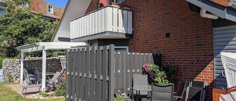 Een achtertuin met een houten terras, een pergola, zitplaatsen buiten en een stenen huis.