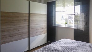 Ein Schlafzimmer mit Bett, einem Fenster mit Aussicht und einem Kleiderschrank mit Holzpaneel-Optik.