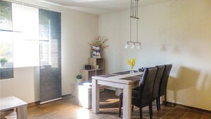 Ein Essbereich mit einem weißen Tisch und Stühlen, einem kleinen Beistelltisch mit einer Vase und einem Fenster mit Jalousien.