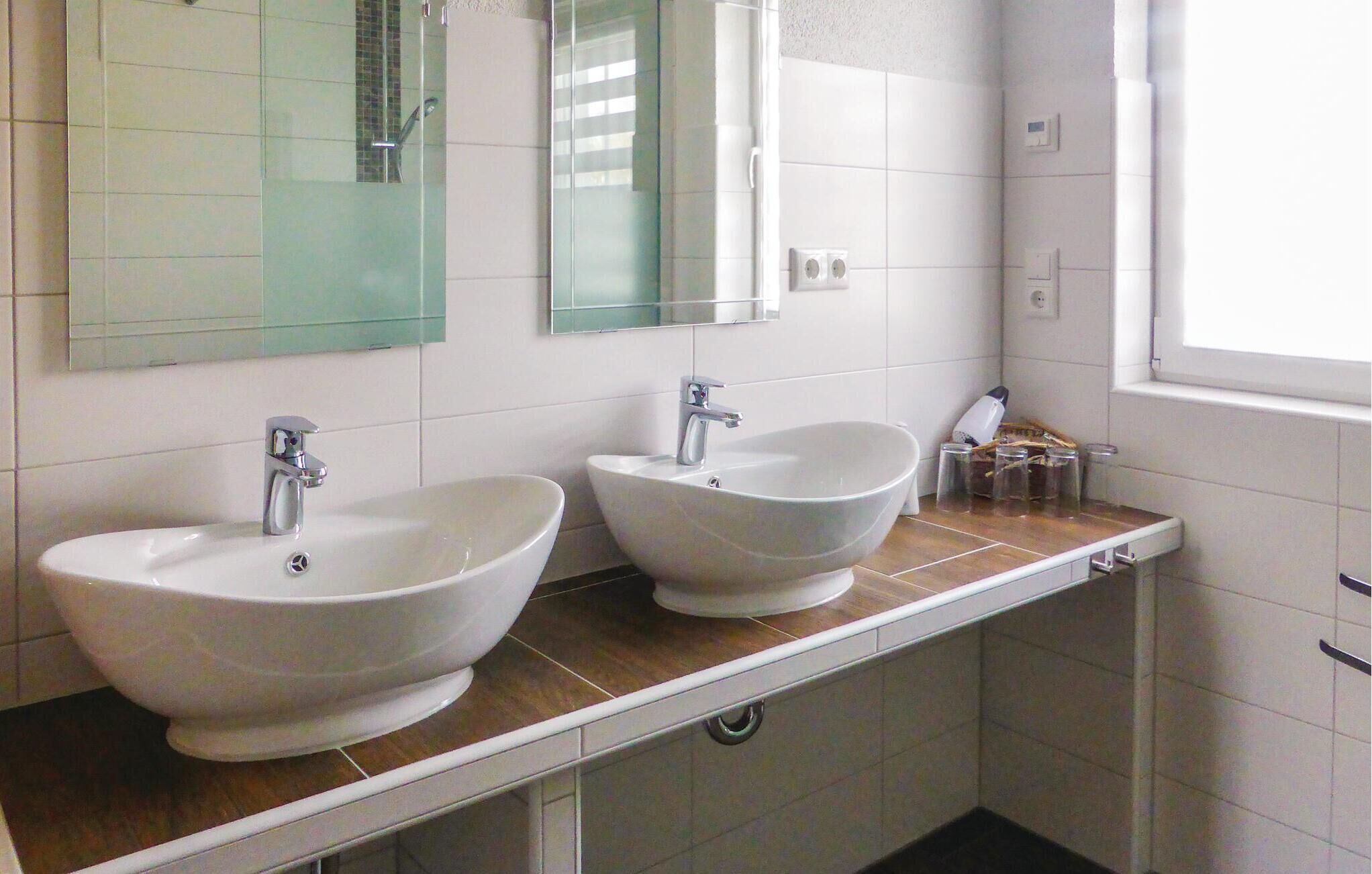 A bathroom with two white sinks, a mirror, and a window.
