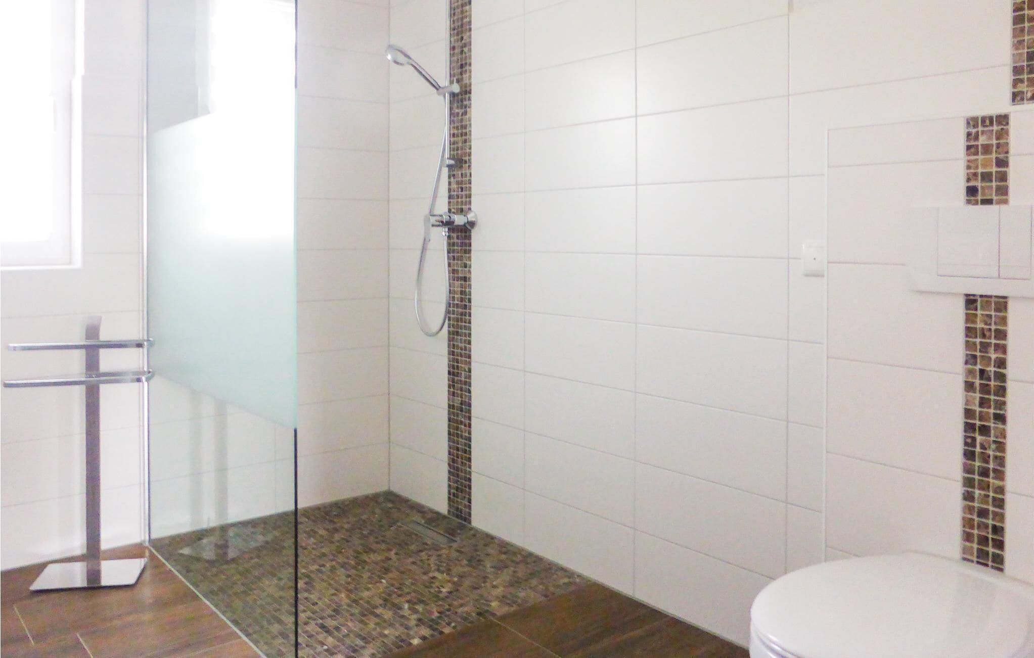 Une salle de bain avec une douche à parois de verre, des toilettes blanches et un carrelage au sol.