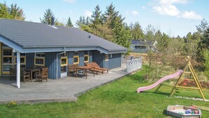 En tvåvåningsbyggnad med en täckt uteplats, utomhusmöbler och en lekplats med en rutschkana.