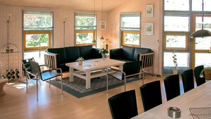 Ett modernt vardagsrum med en svart soffa, ett vitt soffbord och svarta stolar. Det finns stora fönster med utsikt över grönområden.