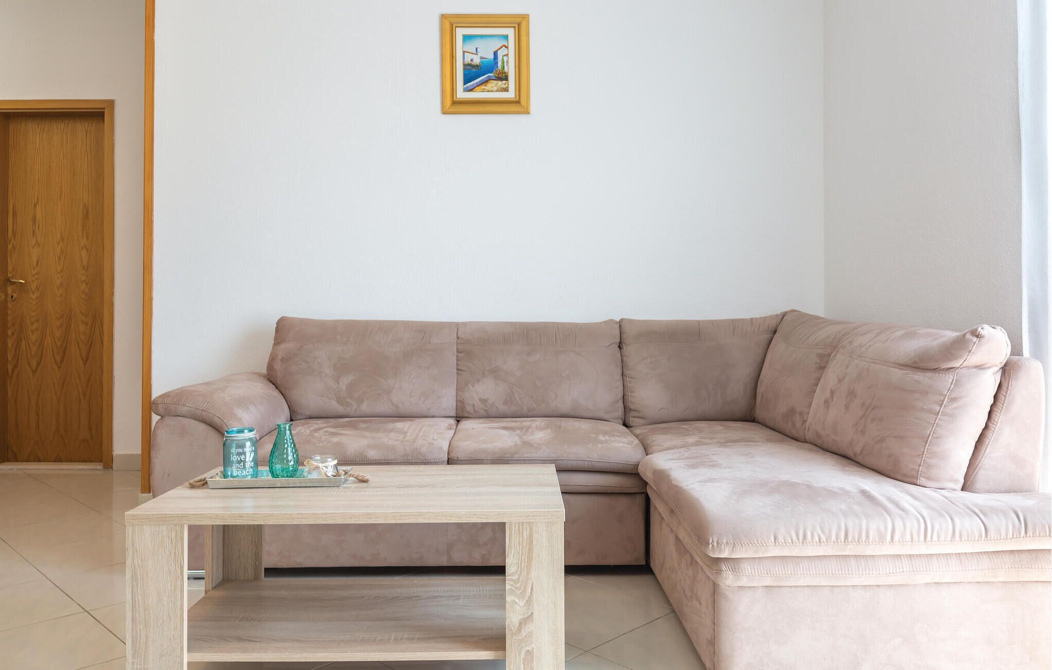 A beige sofa with a wooden coffee table in front, a framed picture on the wall, and a wooden door to the left.