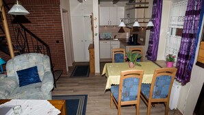 Een compacte leefruimte met een eethoek, keuken en een trap naar een zolderverdieping.