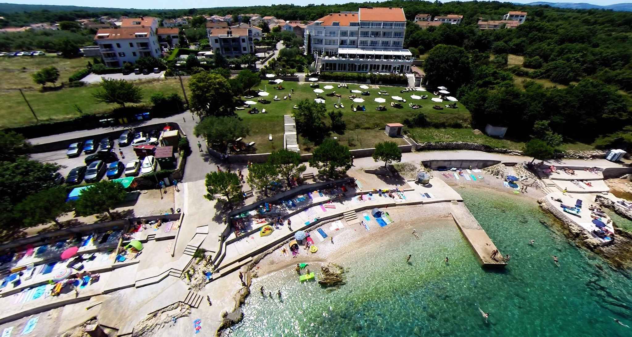 Ein Luftbild eines Küstenresorts mit Strand, klarem Wasser und einem Parkplatz.