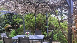 Een terras met een tafel en stoelen, omgeven door groen en een pergola.