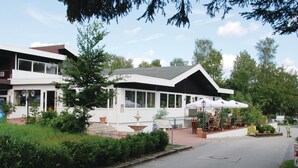 Ein modernes Gebäude mit weißer Fassade, großen Fenstern und einer Außenbereich-Sitzgelegenheit mit Sonnenschirmen.