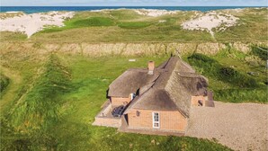 A house with a thatched roof, surrounded by grassy dunes and a beach. - Lovely home in Ringkøbing with sauna (Ringkøbing)