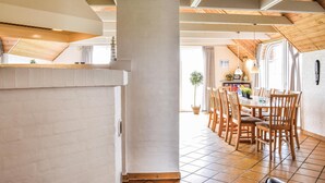 A dining area with wooden chairs and a table, a kitchen area with a stove and cabinets, and a large window providing natural light. - Lovely home in Ringkøbing with sauna (Ringkøbing)