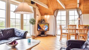 A cozy living room with a leather sofa, wooden dining table, and chairs. A television is mounted on the wall, and there is a window with curtains. - Lovely home in Ringkøbing with sauna (Ringkøbing)