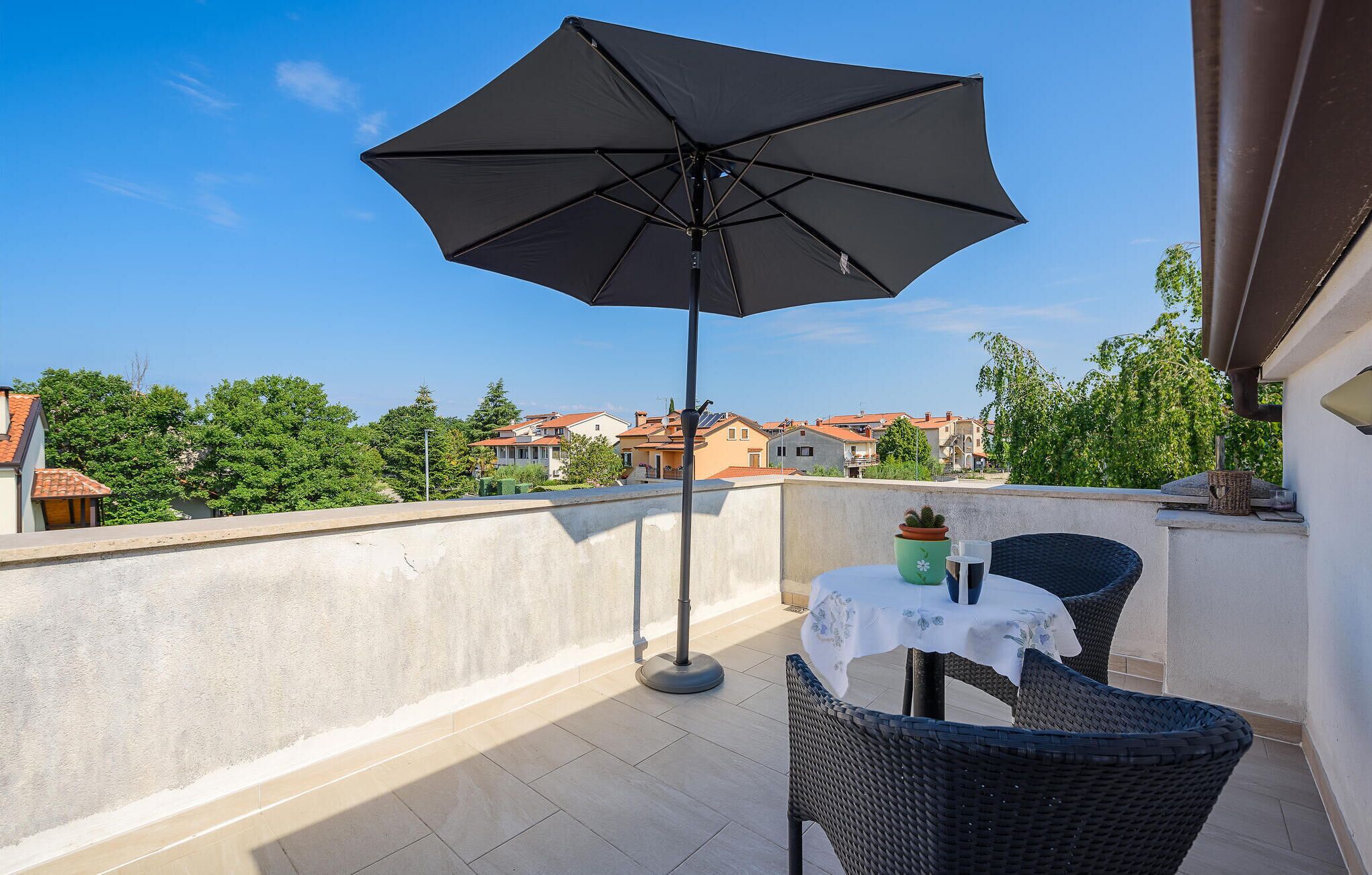 A balcony with a table and chairs, a large umbrella, and a view of surrounding buildings.