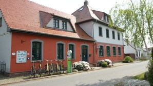 A two-story building with a red roof and white walls, featuring a row of bicycles parked outside. - 5 Kontor - Holiday home Alte Molkerei (Rankwitz)