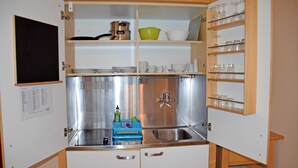 A compact kitchen with a sink, a stove, and shelves above the counter. - 01 Apartment - Ferienhof auf Rügen (Putbus)