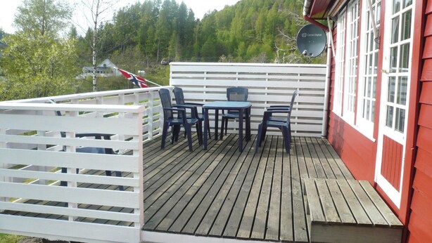 Een houten terras met een witte omheining, een tafel en vier stoelen.