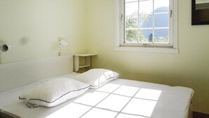 Een eenvoudige, schone kamer met een bed, een raam en een klein plankje.