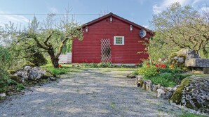 Een rode houten woning met een grindpad dat erheen leidt, omringd door groen en rotsen.