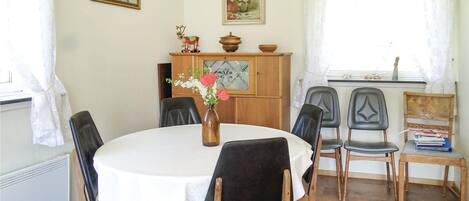 A dining area with a round table, black chairs, a vase with flowers, and wooden cabinets.