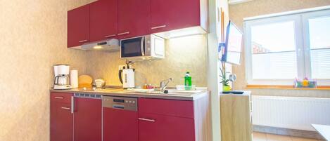 A compact kitchen with red cabinets, a microwave, a coffee maker, and a dishwasher.