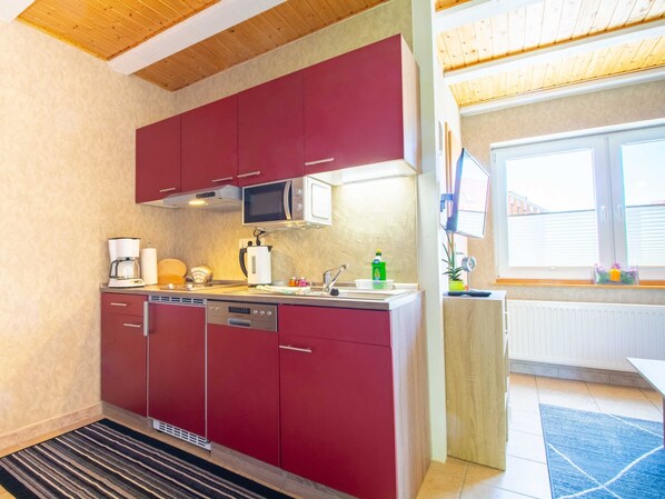 A compact kitchen with red cabinets, a microwave, a coffee maker, and a dishwasher.