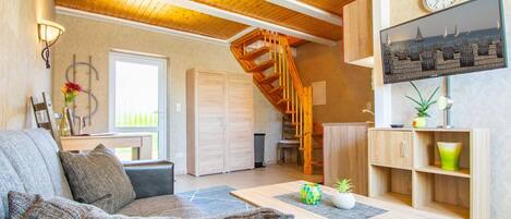 Un salon chaleureux avec un plafond en bois, un escalier, un téléviseur et une vue sur la mer.
