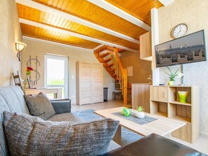 A cozy living room with a wooden ceiling, a staircase, a TV, and a view of the sea.
