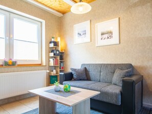 Ein gemütliches Wohnzimmer mit einem grauen Sofa, einem Holztisch und einem Bücherregal mit diversen Gegenständen.