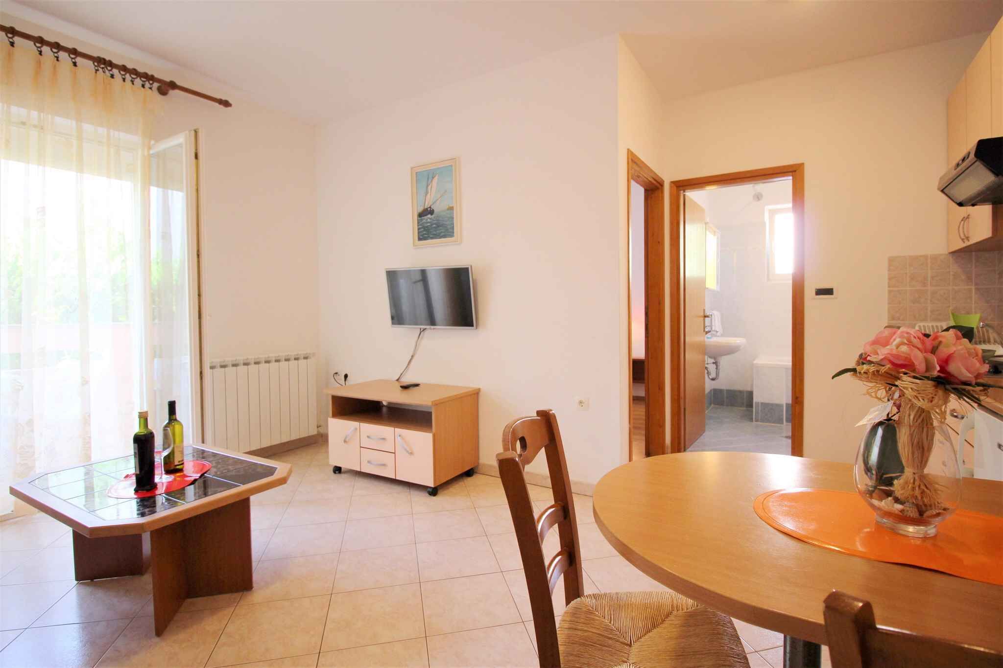 A dining area with a glass-top table, wooden chairs, a TV on the wall, and a view into the adjacent bathroom.